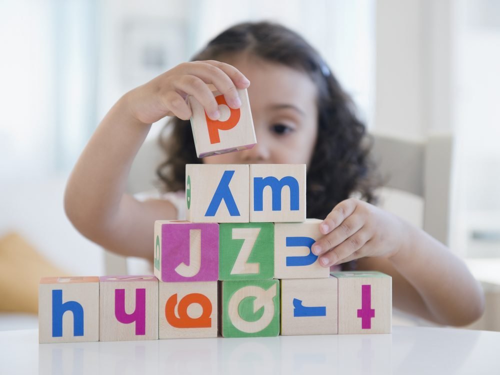 A young child stacking coloured alphabet blocks
